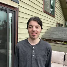 Guy with short hair in gray shirt standing outside