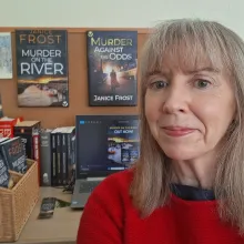 The image  shows the author with some of the covers of her books displayed in the background