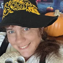 A woman in a witch's hat with a pumpkin behind her