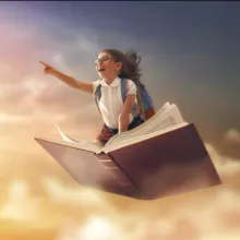 A child on top of a book flying to represent her imagination running free