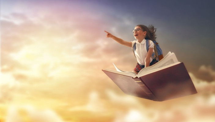 A child on top of a book flying to represent her imagination running free